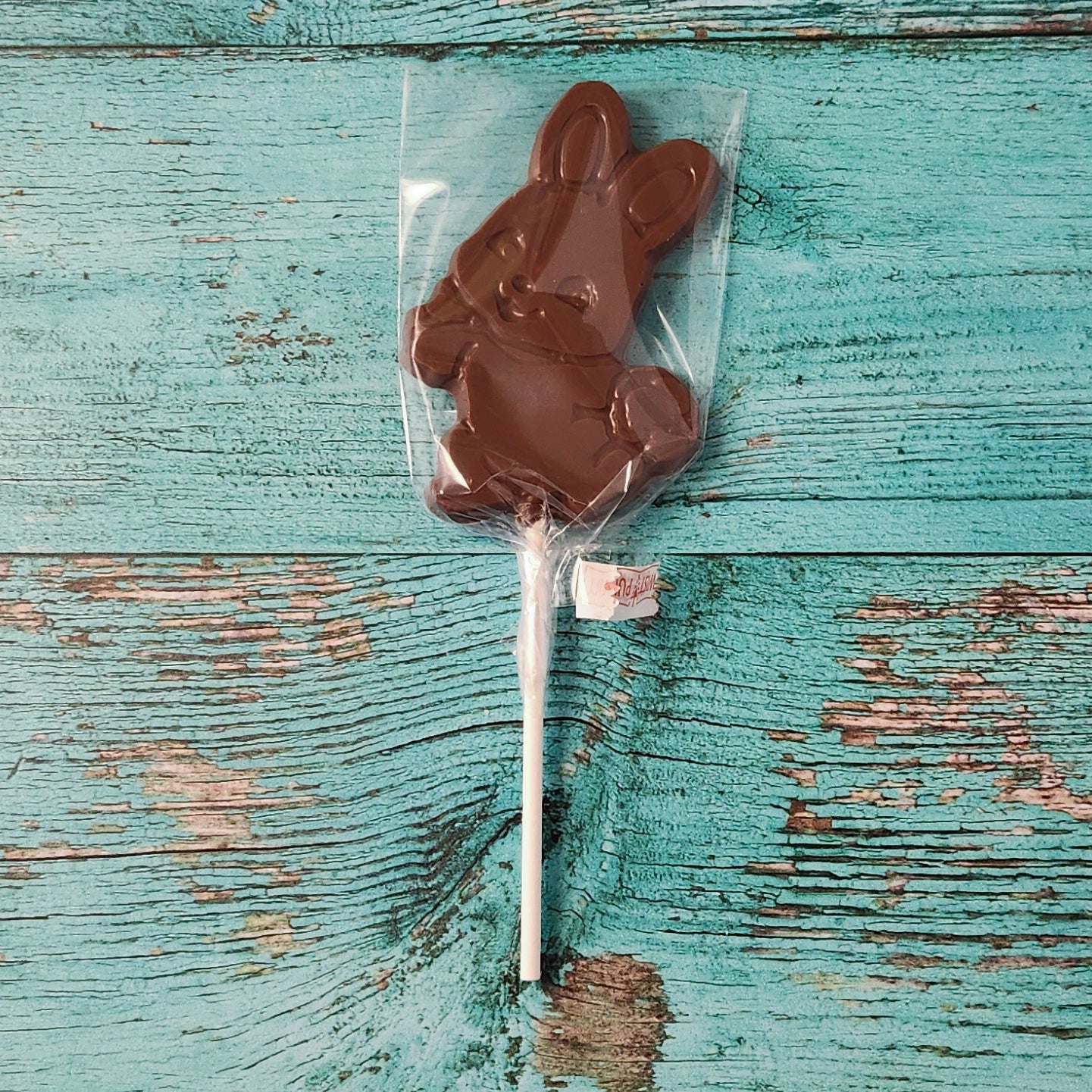 Chocolate bunny on a stick in clear packaging on a rustic wooden surface