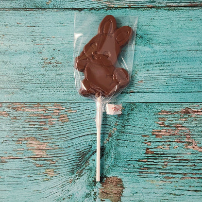 Chocolate bunny on a stick in clear packaging on a rustic wooden surface
