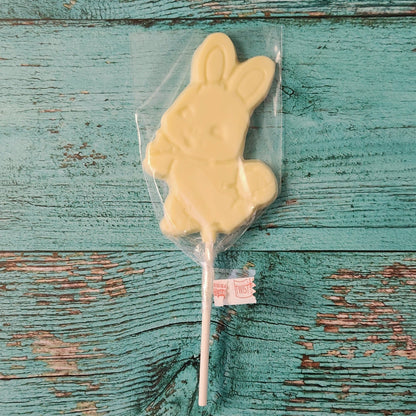 White chocolate bunny on a stick in clear packaging on a rustic wooden surface
