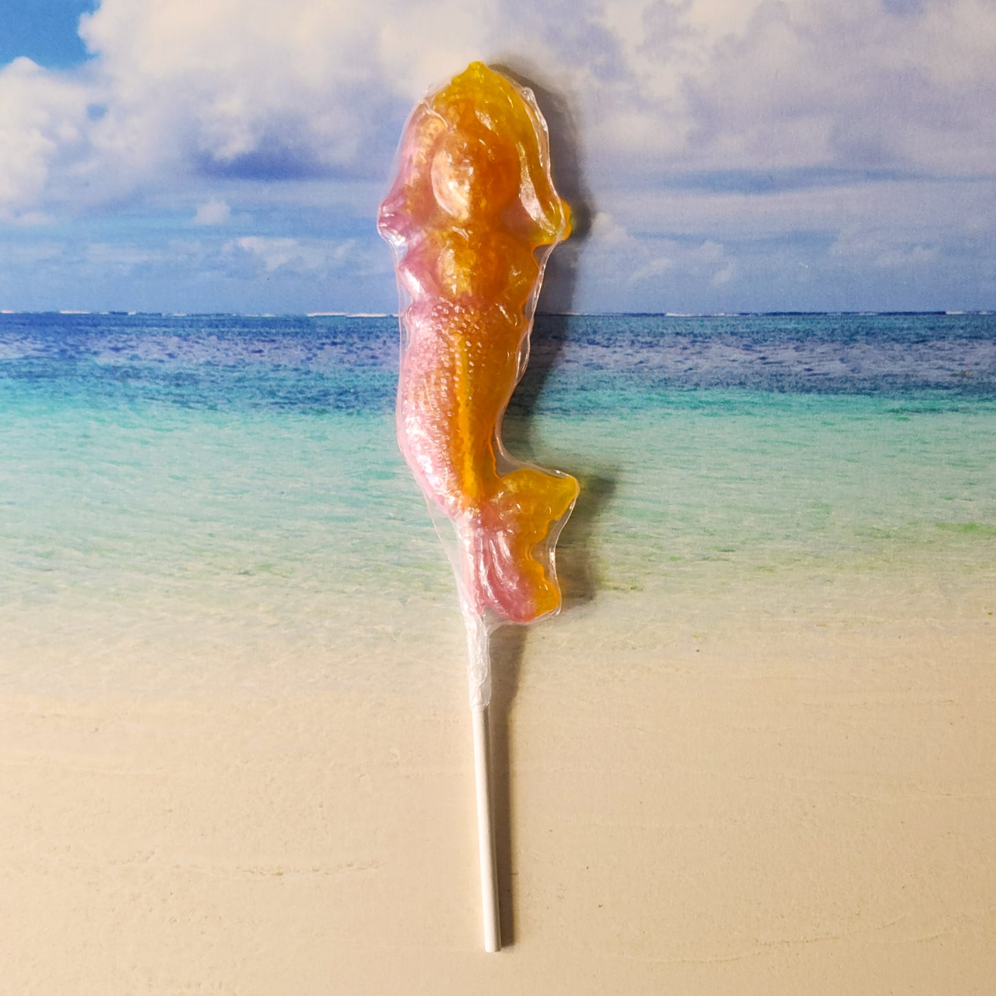 A hard candy lollipop in the shape of a mermaid. Sparkles in Yellow and Pink. The flavor is Strawberry Banana.