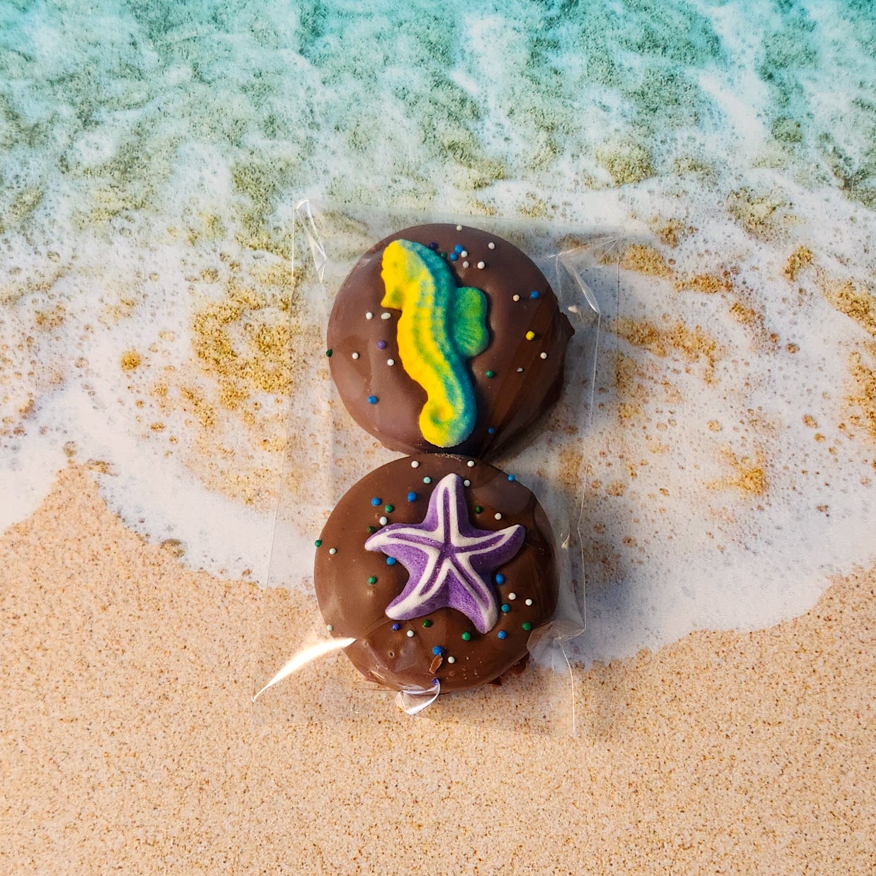 Two milk chocolate covered oreos packaged in a clear bag. Each oreo is decorated with nonpareils and a summer themed sugar decoration.