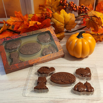 Dive into a box of delicious solid milk chocolates featuring Thanksgiving-themed shapes like Cornucopia, Turkey, Pumpkin, Harvest Stalks, and a 'Happy Thanksgiving' medallion.