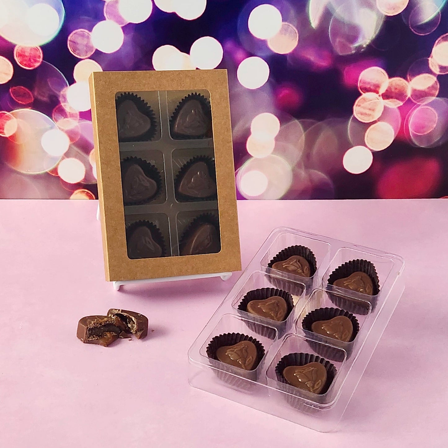 Heart-shaped chocolate candies in a kraft box and clear plastic packaging on a blurred lights background.