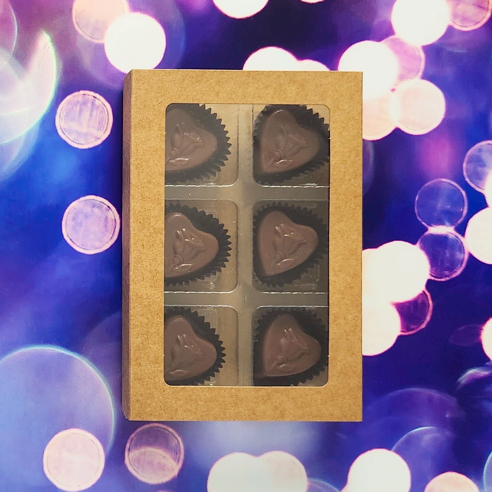 Box of heart-shaped chocolates on a purple background with valentine's day lights