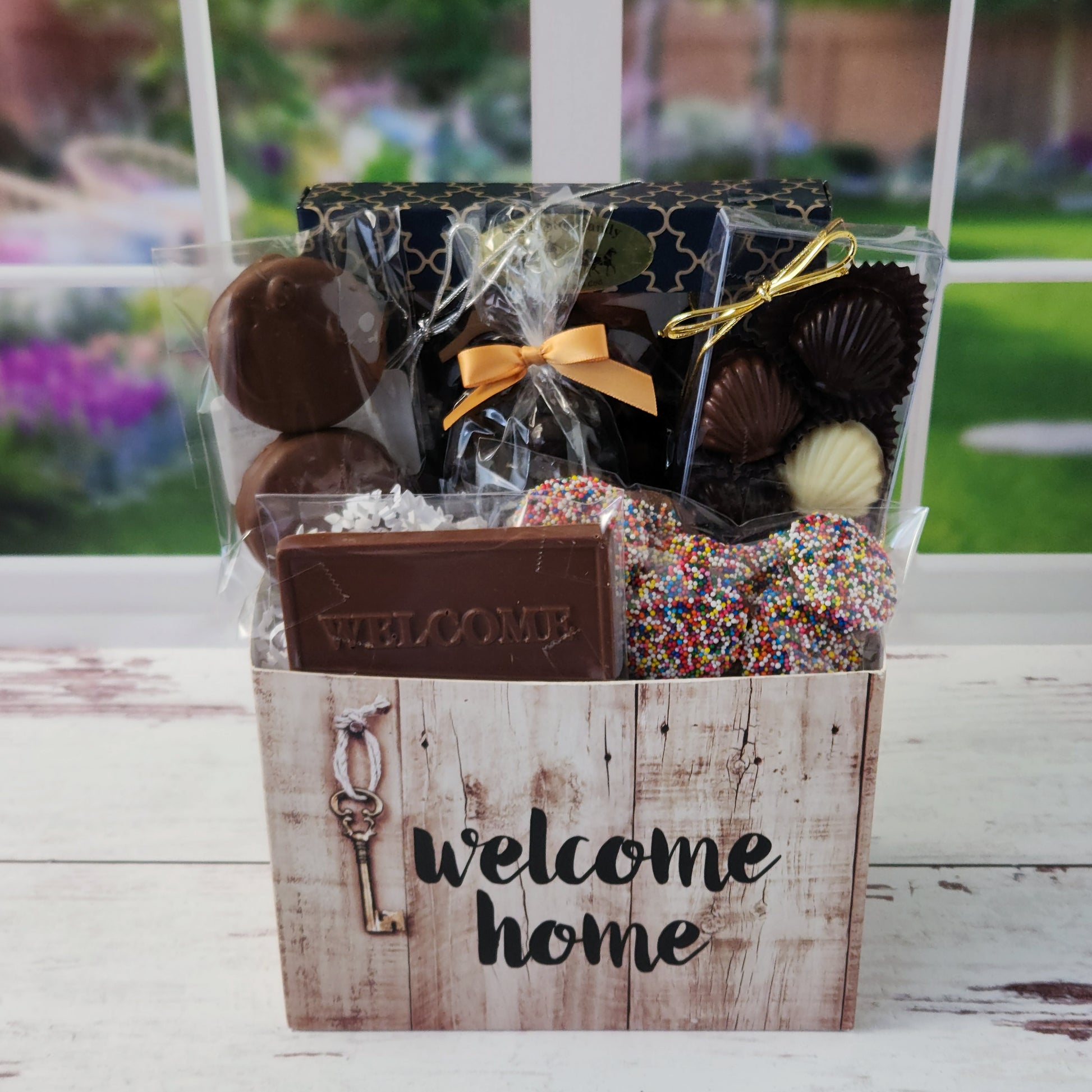 Our Welcome Home Gift Basket is filled with thoughtful treats including: 
Milk, Dark & White Chocolate Sea Shells,  Milk Chocolate Nonpareils,  Dark Chocolate Covered Cranberries,  Two Chocolate Covered Oreos, a "Welcome" Milk Chocolate Bar and a 16-Piece Chocolate Assortment – filled with creams, caramels, meltaways, and truffles.  All overwrapped with a bow and ready for gifting.