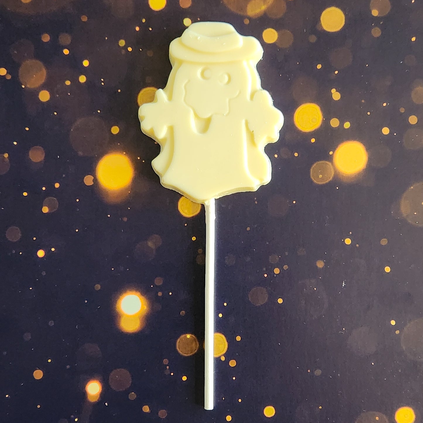 White Chocolate Ghost with hat Lollipop.  Measuring approximately 2.75 inches wide by 3.25 inches tall (excluding the pop stick)