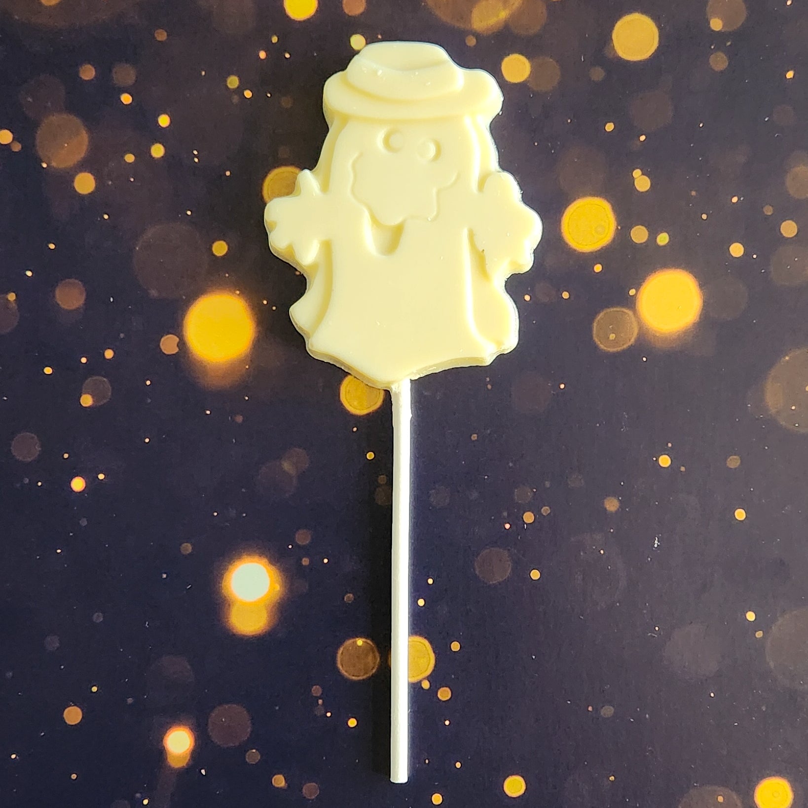 White Chocolate Ghost with hat Lollipop.  Measuring approximately 2.75 inches wide by 3.25 inches tall (excluding the pop stick)