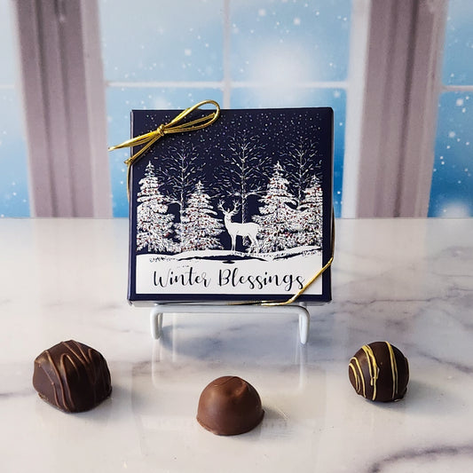 An assortment of our most popular milk and dark chocolate creams, caramels, melt-aways, and truffles all packed inside a box with a deer in the forest and the words "Winter Blessings" printed on the cover.