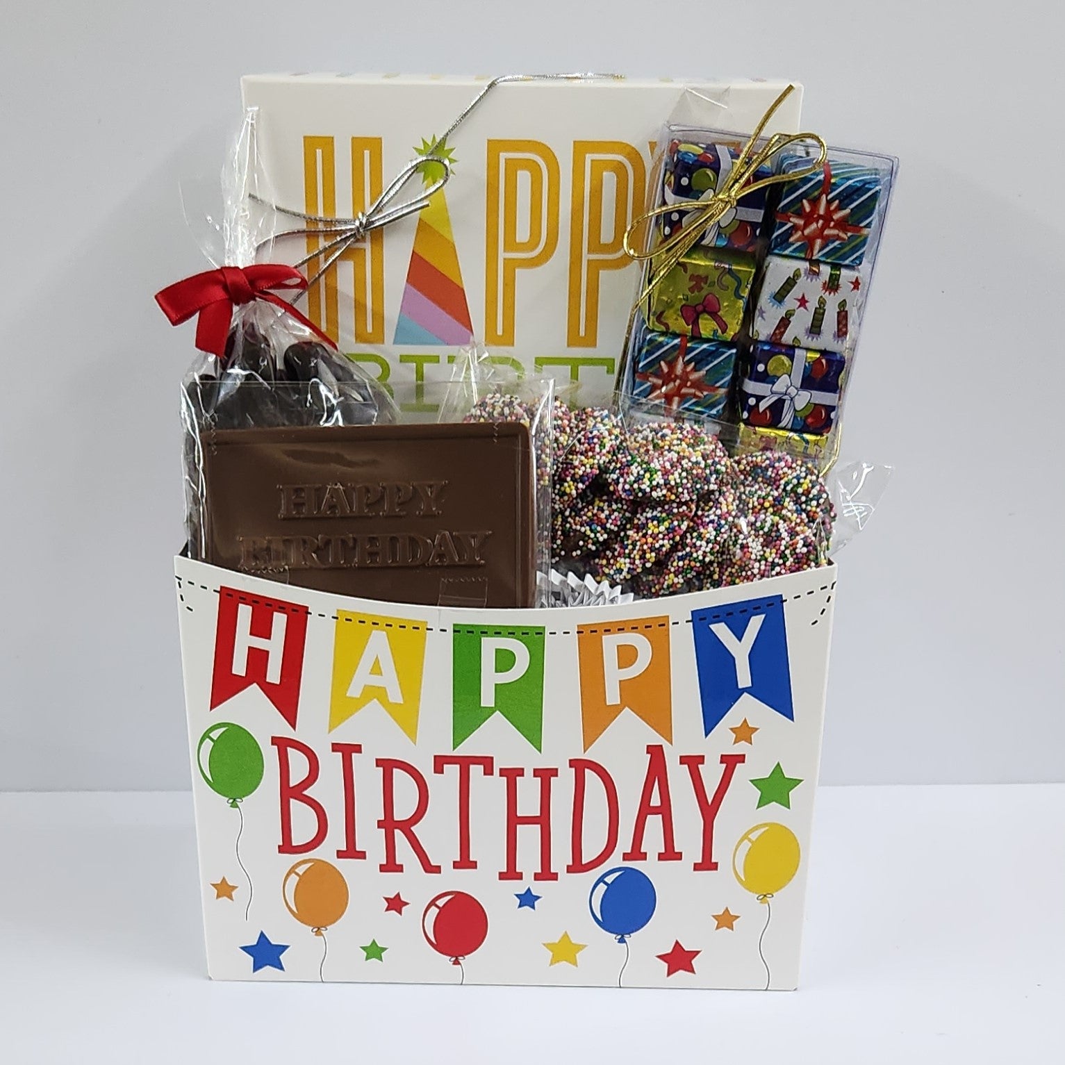 Happy Birthday Gift Basket with balloon images includes foiled milk chocolate presents, milk chocolate nonpareils, dark chocolate-covered cranberries, milk chocolate birthday card and a 16-piece cream, caramels, meltaways, and truffle assortment