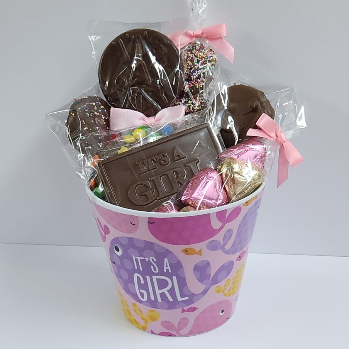 It's a Girl Gift Basket includes Milk Chocolate Nonpareils, Milk Chocolate covered Oreos, Shortbread Cookies, and a M&M-covered pretzel, pink foiled milk chocolate hearts and a special milk chocolate card and lollipop that say "It's a Girl!".