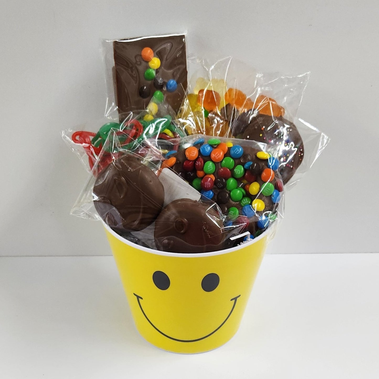 Smile Gift Basket includes Milk Chocolate covered Oreos and Shortbread Cookies, a crunchy M&M Pretzel, M&M Milk Chocolate Fun Bar, 12 flavor Gummi Bears, and chewy Rainbow Laces inside a yellow smiley face bucket